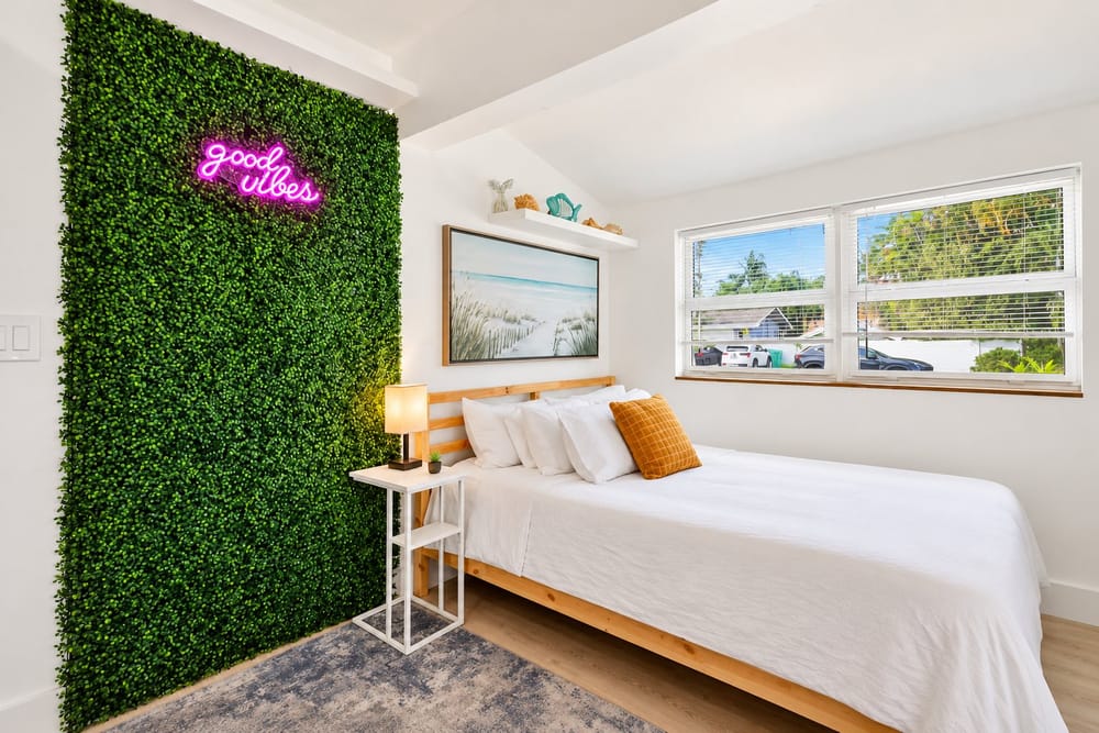 Bright coastal bedroom with a living green wall and a "good vibes" neon sign, a home BookedMore co-hosts